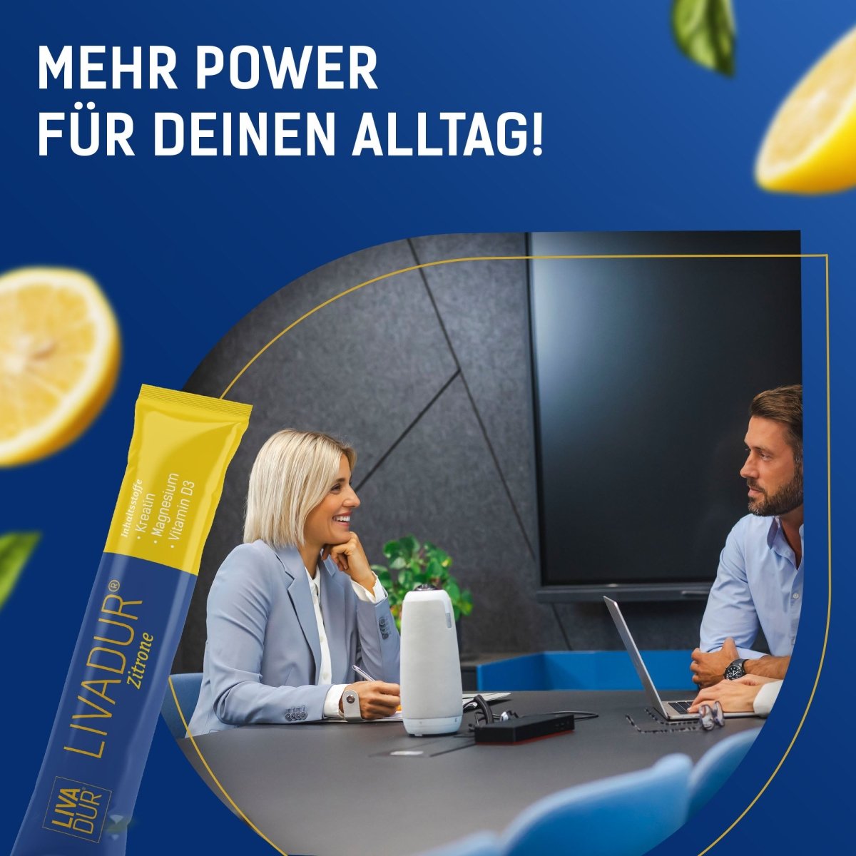 Two people sit at a conference table with laptops, smiling. In the foreground is a yellow LIVADUR® Tagesstick (Zitronengeschmack, 30 Stück/Packung). Lemons are in the corners. Text reads: MEHR POWER FÜR DEINEN ALLTAG!.