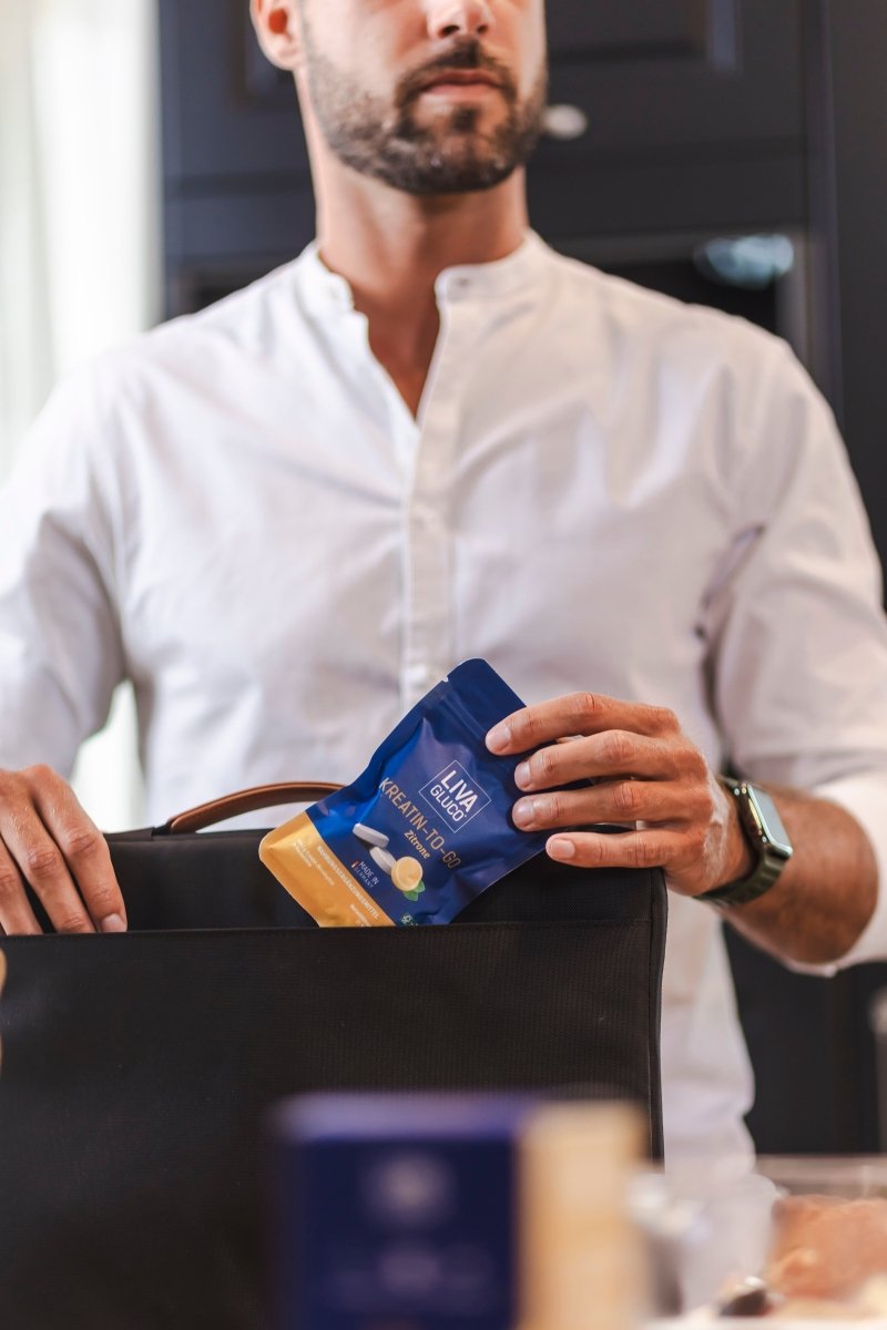 A man in a white shirt places a blue and yellow LivaGluco® snack pouch into a black bag. His face is partially visible, and he wears a smartwatch on his left wrist.
