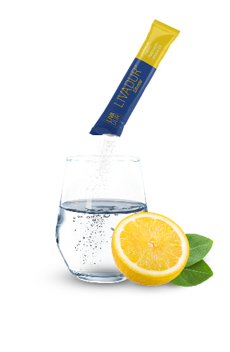 A glass of water with a yellow LIVADUR powder packet being poured in, beside a half lemon and two green leaves—ideal for your Trinkflasche or as part of your monthly Christmas Bundle routine.
