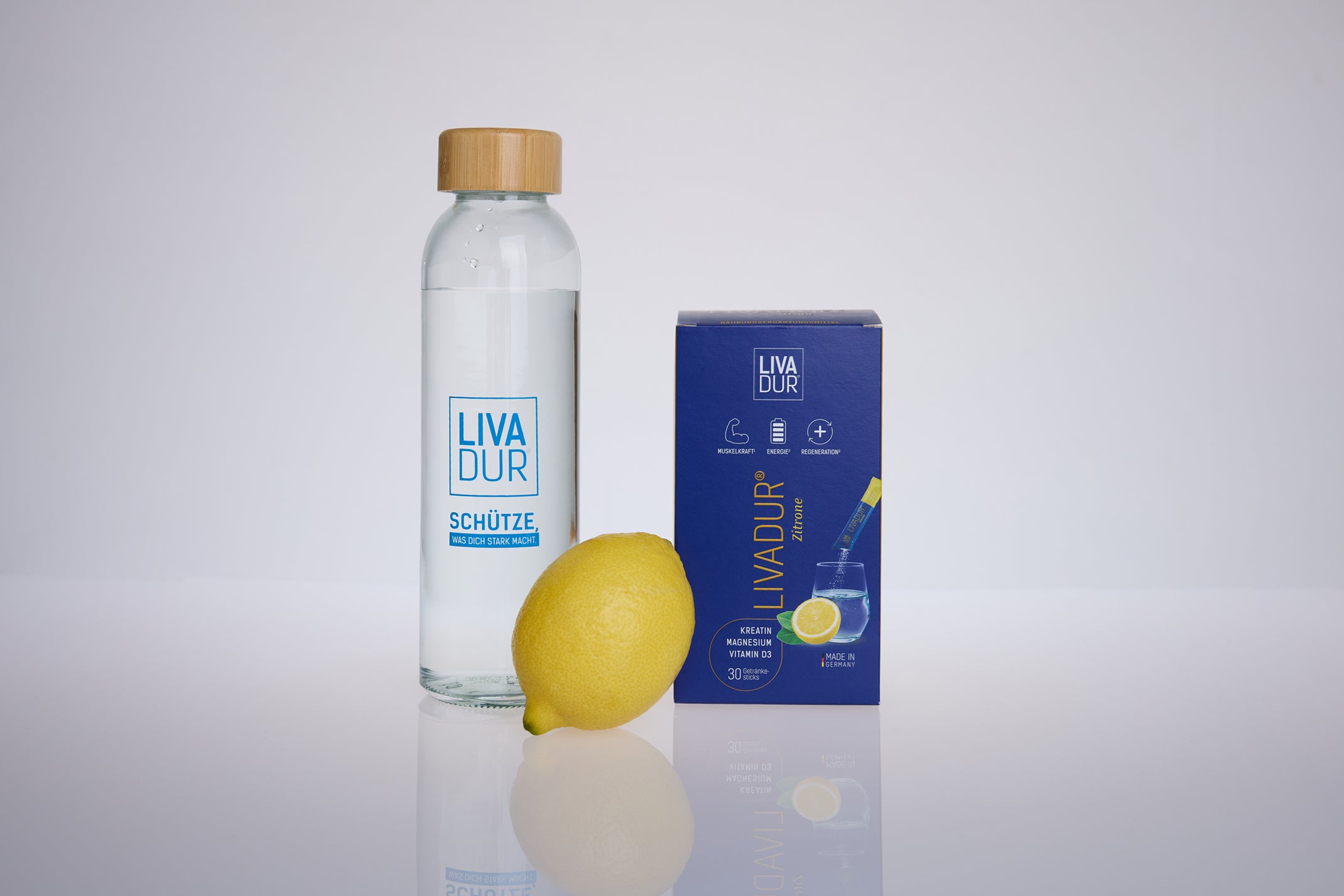A glass bottle of water, a blue Blackweek Bundle box, and a fresh lemon are arranged on a white surface with a light background.